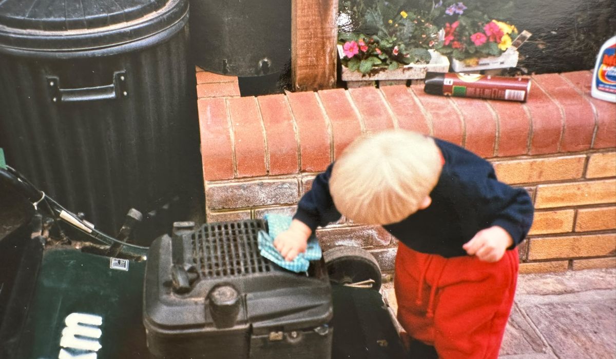 Toddler wiping down a lawn mower with a cloth, playfully helping to clean garden equipment.