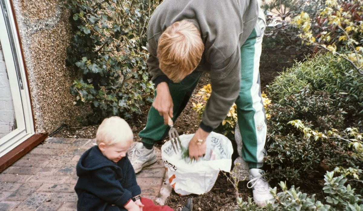 Adult tending a garden border while a young child sits nearby, learning about gardening from an early age.