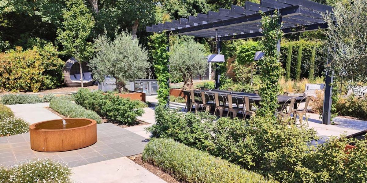 A serene garden featuring a wooden pergola and a table set for outdoor dining. 