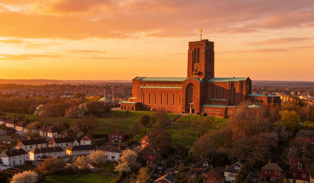 A large red-brick structure sits atop a grassy hill overlooking a residential neighborhood at sunset.