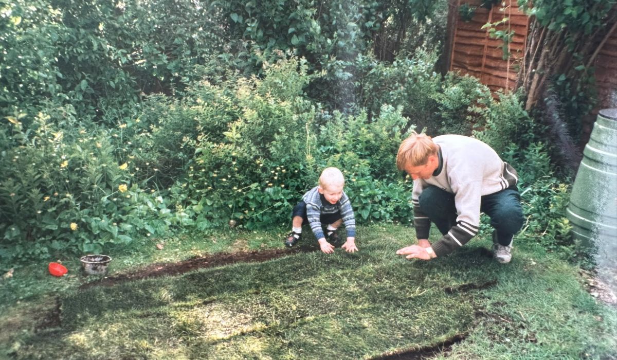 Adult and young child laying fresh turf together in a garden during an early landscaping project.