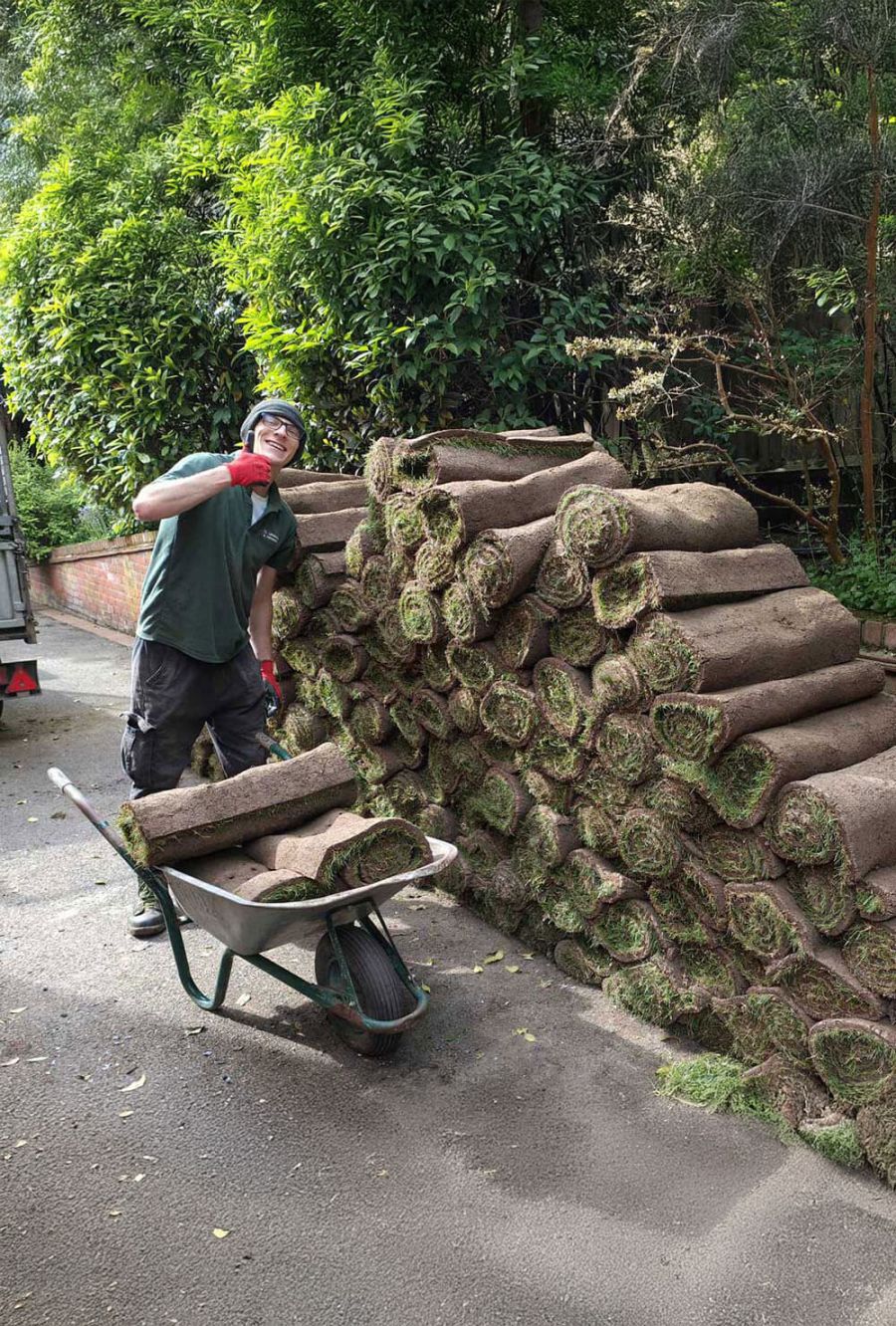 A man pushing a wheelbarrow filled with freshly cut grass across a grassy area.  