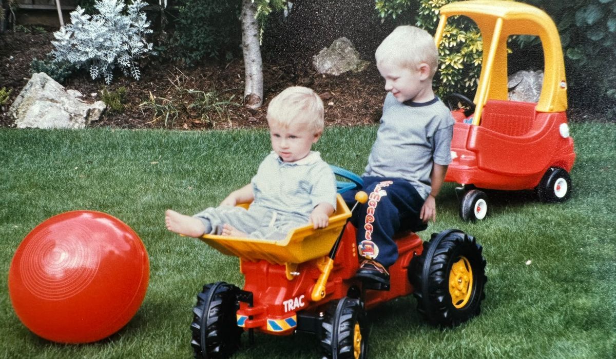 Two young children playing on toy garden vehicles in a well-kept lawn, reflecting an early passion for landscaping.